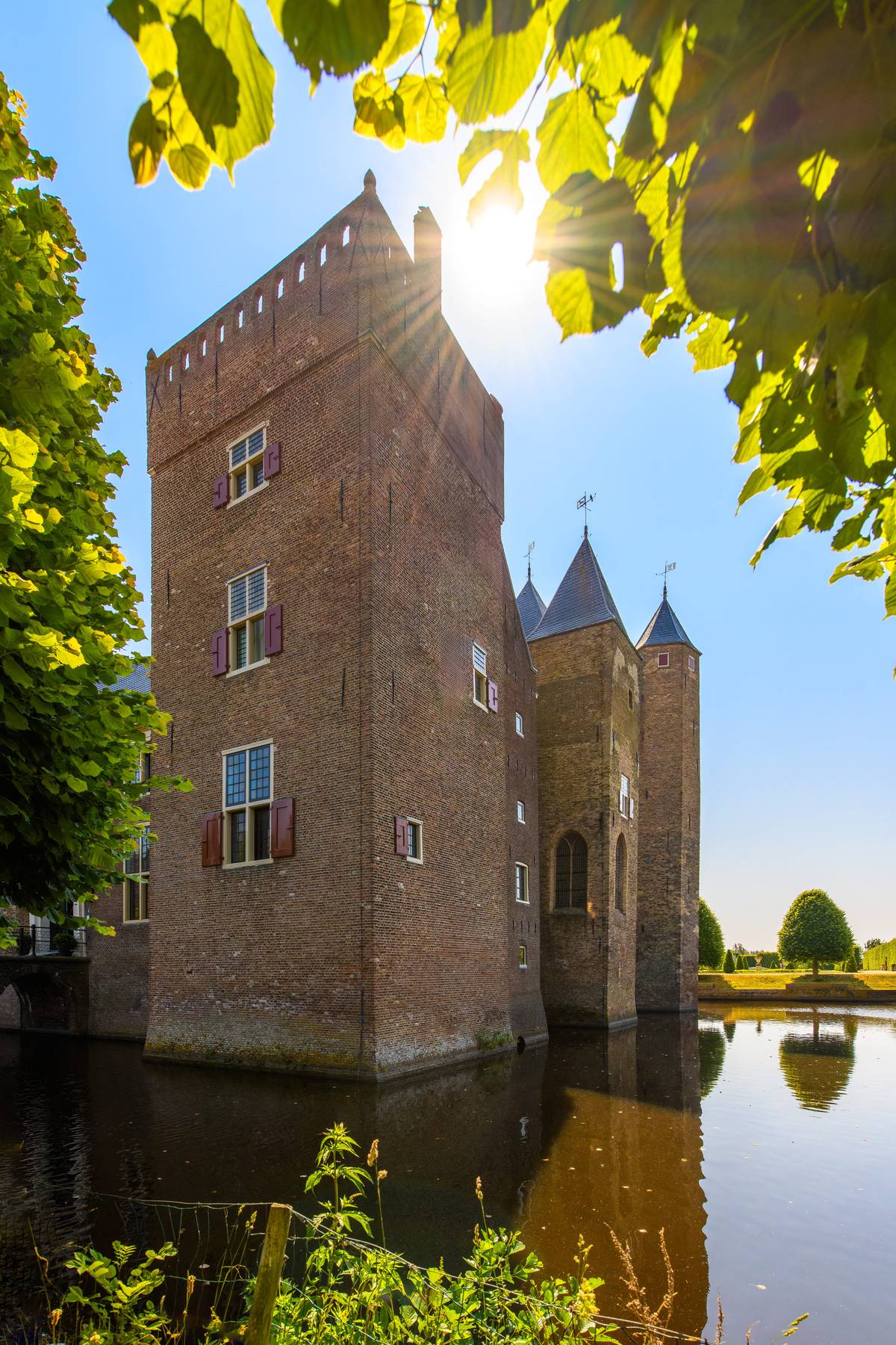 Slot Assumburg in Heemskerk, gezien door de bladeren met de zon achter de toren.