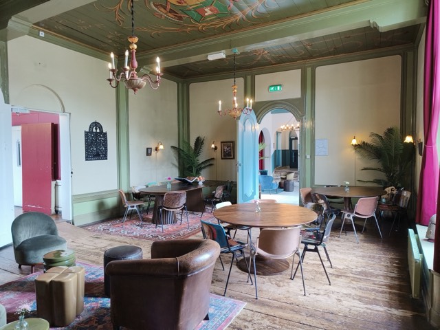 De Deutzzaal: groen geschilderde lambrisering, een beschilderd plafond met wapenschilden en leren fauteuils op een houten vloer.