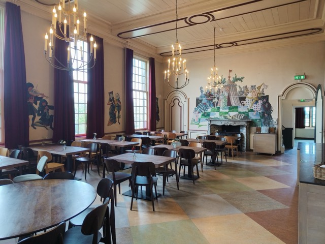 De Geverszaal: hoge zaal met muurschilderingen van middeleeuwse muzikanten en een grote schouw.